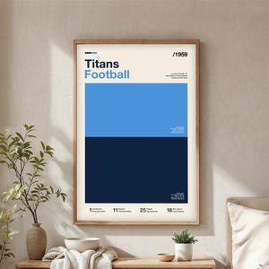 May include: A framed poster with a minimalist design featuring the words "Titans Football" in blue. The poster has a light blue and navy blue colour block design. The year "/1959" is at the top. The poster includes text at the bottom indicating "1 Conference Championships, 11 Division Championships, 25 Playoff Appearances, 18 NFL Hall of Fame Players."