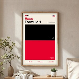 May include: A framed poster with a minimalist design featuring the text "Haas Formula 1." The poster is divided into black and red sections. The American flag is in the upper right corner. Additional text includes "VF-25," "Ferrari," and "2016."