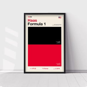 May include: A framed poster featuring the Haas Formula 1 team. The design is split into black and red sections with the team name in bold red letters. The American flag is in the top right corner. The poster includes the text "VF-25", "Ferrari", and "2016".