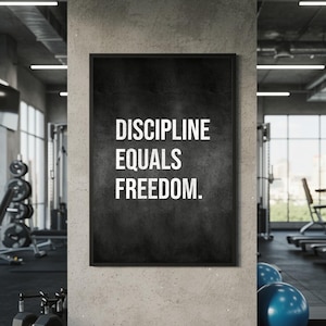 以下が含まれることがあります： 黒いフレームのポスター。白い文字で「DISCIPLINE EQUALS FREEDOM」と書かれており、暗く質感のある背景が特徴です。ジムを背景に、エクササイズ器具が見えます。