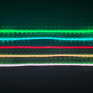 May include: Five different colored LED light strips, green, blue, red, yellow, and white, are laid out horizontally on a black surface.