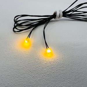 May include: Two yellow LED lights connected by a black wire. The lights are turned on and glowing.