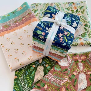 May include: A collection of patterned fabric bundles. The fabrics feature floral, mushroom, and owl designs in various colors, including blue, green, and peach. A white ribbon wraps around a stack of the fabric bundles.