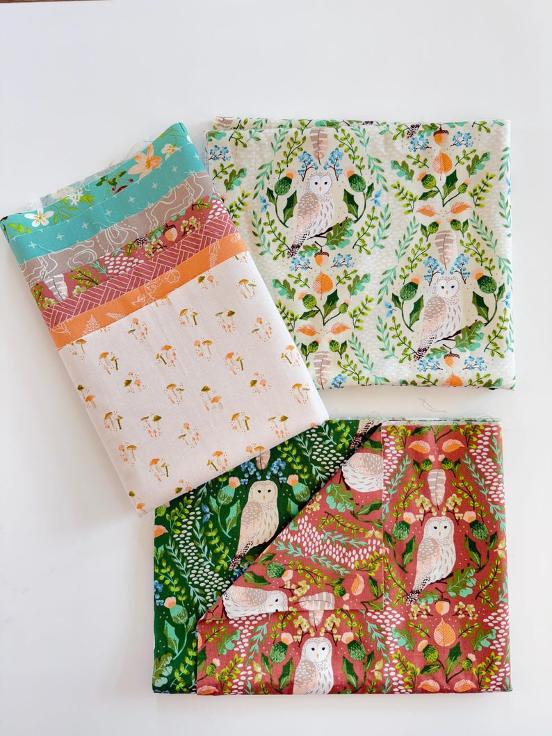 May include: Several folded fabric pieces with various patterns are displayed. One features mushrooms, another has owls and foliage, and others have floral and geometric designs. The color palette includes teal, orange, pink, and green.