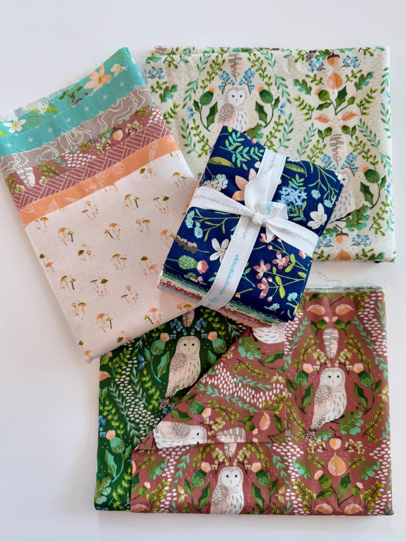 May include: A collection of fabric bundles with various floral and woodland patterns. The fabrics feature designs with mushrooms, owls, and botanical elements in shades of teal, pink, and navy, tied with a white ribbon.