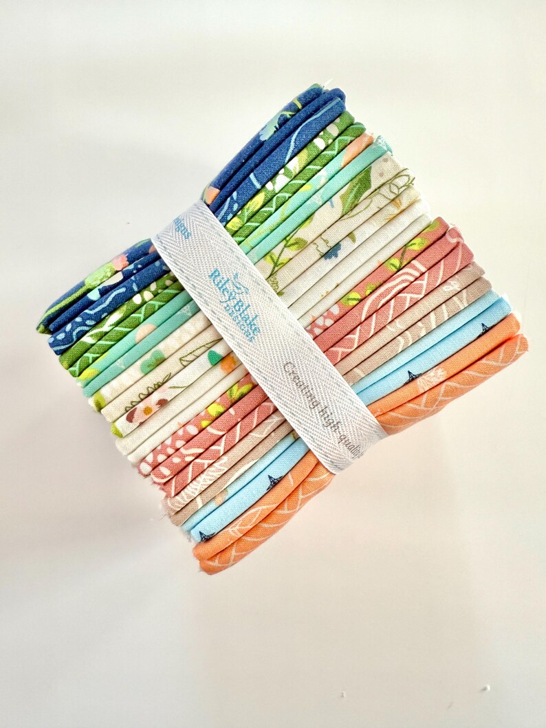 May include: A stack of colorful fabric squares, bound with a white ribbon. The fabric features floral and geometric patterns in shades of blue, green, pink, and orange. The ribbon is printed with "Riley Blake Designs" and "Creating high-quality".