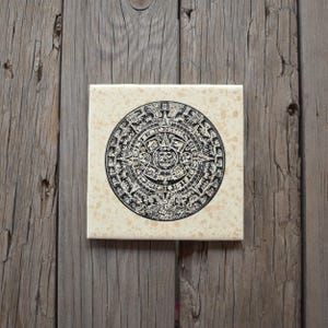 May include: Square tile featuring a black and white depiction of the Mayan calendar. The circular design is centered on a beige background with a speckled pattern. The tile is displayed on a weathered wooden surface.