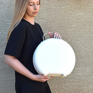 May include: A white round hard-sided suitcase with a handle. The suitcase is about 12 inches in diameter.