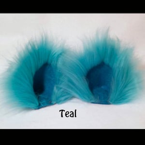 May include: A pair of teal faux fur earmuffs. The earmuffs are made of soft, fluffy fur and have a teal color.