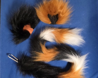Könnte beinhalten: Eine Auswahl an Kunstfellschwänzen in Schwarz, Orange und Weiß. Ein Schwanz hat einen silbernen Verschluss. Die Schwänze sind flauschig und sehen realistisch aus. Die Schwänze sind wahrscheinlich für Cosplay oder Kostüme gedacht.