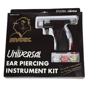 May include: A black and white ear piercing instrument kit. The kit includes a piercing gun and several ear piercing studs. The box has the text "STUDEX Universal Ear Piercing Instrument Kit".