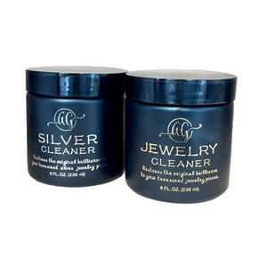 May include: Two dark blue jars of jewelry cleaner. One jar is labeled "SILVER CLEANER" and the other "JEWELRY CLEANER". Each jar contains 236 ml of cleaner and has a logo at the top.