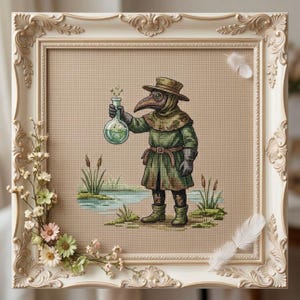 Könnte beinhalten: Eine Kreuzstichstickerei, die einen Pestdoktor in grünem Mantel und Hut zeigt, der einen Glaskolben mit grüner Flüssigkeit hält. Die Figur steht an einem kleinen Teich mit Schilf. Das Kunstwerk befindet sich in einem verzierten cremefarbenen Rahmen.