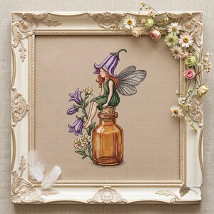 Könnte beinhalten: Eine Kreuzstichstickerei mit einer Fee mit rotem Haar, grüner Kleidung und durchscheinenden Flügeln, die auf einer braunen Glasflasche sitzt. Die Fee trägt eine violette glockenförmige Blume als Hut. Neben der Flasche wachsen Glockenblumen.