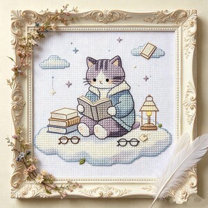 Könnte beinhalten: Eine Kreuzstichstickerei mit einer violett-weißen Katze in einer blauen Jacke, die auf einer Wolke sitzt und ein Buch liest. Die Szene umfasst einen Bücherstapel, eine Laterne, zwei Brillen und Sterne, eingefasst in einen verzierten weißen Rahmen.