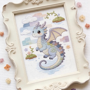 Könnte beinhalten: Kreuzstich-Kunstwerk eines freundlichen, pastellfarbenen Drachen mit blauen, lila und gelben Schuppen, Flügeln und Hörnern. Der Drache ist vor einem Hintergrund aus Wolken, einem Regenbogen und kleinen Inseln mit Blumen platziert. Das Kunstwerk ist in einem weißen Rahmen gerahmt.