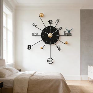 Könnte beinhalten: Eine moderne Wanduhr mit schwarzem Zifferblatt und goldenen Akzenten. Die Uhr hat ein minimalistisches Design mit ausgeschriebenen Zahlen und goldenen Kugeln, die die Stunden markieren. Das Wort "Ingle" steht über einer Hirschsilhouette.