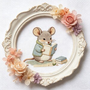 May include: A framed embroidery featuring a charming mouse reading a book. The mouse wears a blue jacket and sits on a green mat. The white frame is adorned with pastel-colored flowers, creating a whimsical, storybook aesthetic.