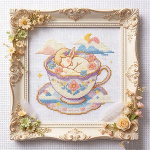 Könnte beinhalten: Kreuzstich-Kunst eines schlafenden Hasen in einer Teetasse, gerahmt mit einem weißen, verzierten Rahmen und floralen Akzenten. Die Tasse und Untertasse sind mit floralen Mustern in Pastellfarben verziert. Der Hase ist weiß mit einer rosa Nase und schläft in einer Teetasse.
