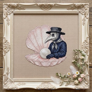 Könnte beinhalten: Eine Kreuzstichstickerei, die einen Pestarzt in einem dunkelblauen Mantel und Hut zeigt, der eine große weiße Perle in einer rosa Muschel hält. Das Kunstwerk befindet sich in einem verzierten, cremefarbenen rechteckigen Rahmen.