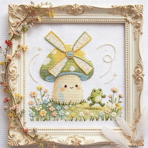 Könnte beinhalten: Eine Kreuzstichstickerei mit einem lächelnden Pilz mit Windmühlenhut, begleitet von einem kleinen grünen Frosch in einem Feld aus bunten Blumen. Das Kunstwerk befindet sich in einem verzierten, cremefarbenen Rahmen, der mit kleinen Trockenblumen geschmückt ist.