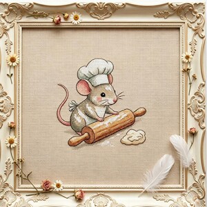 Könnte beinhalten: Eine Kreuzstichstickerei mit einer kleinen Maus, die eine weiße Kochmütze trägt und ein hölzernes Nudelholz auf einem Stück Teig benutzt. Das Kunstwerk befindet sich auf einem beigen Stoffhintergrund in einem verzierten, cremefarbenen Rahmen.
