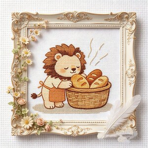 Könnte beinhalten: Eine Kreuzstichstickerei mit einem Löwen in einer orangefarbenen Schürze, der neben einem geflochtenen Korb mit drei Brotlaiben steht. Das Kunstwerk befindet sich in einem verzierten, cremefarbenen Rahmen, der mit kleinen Stoffblumen und einer weißen Feder geschmückt ist.