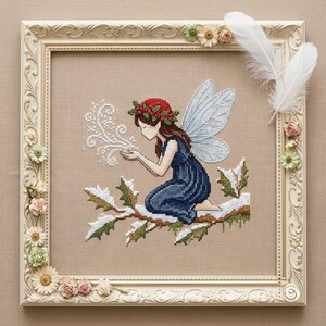 May include: A cross-stitch embroidery of a fairy with brown hair, a red holly berry crown, and blue wings, kneeling on a snow-covered branch. The fairy wears a dark blue dress and blows white sparkles. The piece is in an ornate cream frame with flowers.
