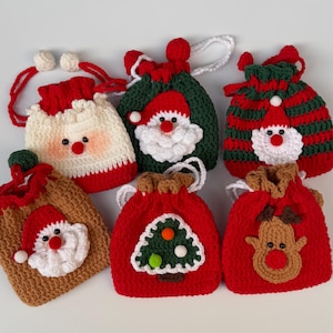 May include: A collection of six handmade crochet Christmas gift bags. The bags feature festive designs, including Santa Claus faces, a Christmas tree, and a reindeer. The bags are primarily red, white, green, and brown, with drawstring closures.