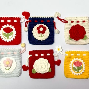 Puede incluir: Seis bolsas de crochet hechas a mano con cordón en varios colores: rojo, azul, blanco, gris, rojo y amarillo. Cada bolsa presenta un diseño floral en el centro, con un cordón a juego y detalles decorativos. Ideales para pequeños regalos o almacenamiento.