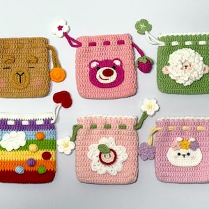 May include: A collection of six handmade crochet drawstring pouches in various colors and designs. Each pouch features a unique character or pattern, including a bear, a sheep, and a rainbow. The pouches have decorative pulls and are suitable for small items.