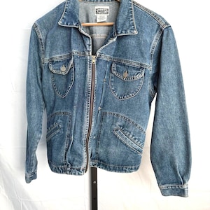 May include: A light blue denim jacket with a zip-up front, two chest pockets, and two lower pockets. The jacket has a collar and long sleeves. The brand name "ROSE" is visible on a tag inside the jacket.