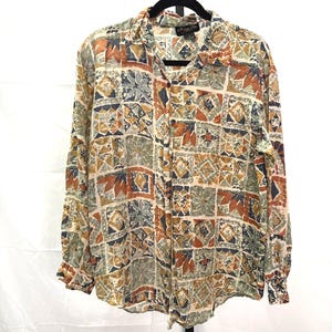 May include: A long-sleeved button-down shirt with a colorful geometric pattern. The shirt features a collared neckline and buttoned cuffs. The pattern includes squares, triangles, and leaf shapes in shades of beige, brown, green, and blue.