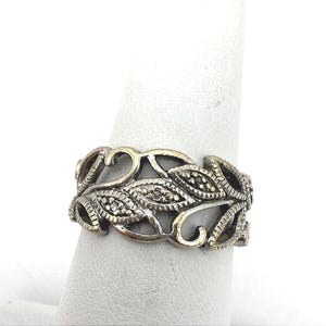 May include: A silver-toned metal ring featuring an openwork design of interconnected leaves and swirling vine-like patterns. The surface of the leaves displays a textured, stippled finish, while the edges of the band have a polished metallic sheen.