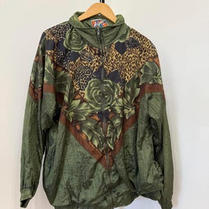 May include: Green vintage windbreaker jacket with a floral and animal print design. The jacket features a high collar, a full zipper, and brown accents. The floral pattern includes roses and leaves, with leopard print accents.