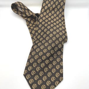 May include: A brown necktie with a repeating pattern of light tan leaf-like shapes. The tie is knotted and lies on a white surface. The tie is made of a smooth fabric.