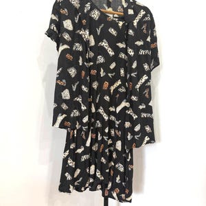 May include: Black dress and matching short-sleeved jacket set. The fabric features a repeating pattern of various shoe designs in white, tan, and brown. The dress hangs on a wooden hanger against a white background.
