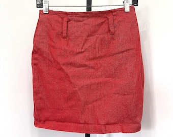 Può includere: Una minigonna in denim rosso tinta unita caratterizzata da una vita strutturata con passanti per cintura, un orlo dritto e una classica struttura a cinque tasche, esposta su una gruccia di plastica nera su uno sfondo bianco.