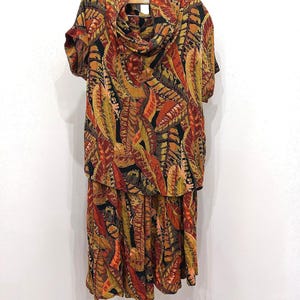 May include: A two-piece set consisting of a short-sleeved top with a cowl neckline and a matching skirt, both featuring an all-over print of overlapping tropical leaves in shades of burnt orange, mustard yellow, and deep black.