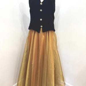 May include: A two-piece ensemble featuring a black velvet halter-style waistcoat with four round, decorative buttons down the front, paired with a floor-length, full-skirted gold organza skirt that has a sheer, layered appearance and a subtle shimmer.
