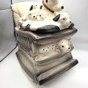 May include: A ceramic Dalmatian dog figurine with a mother dog and puppies. The dogs are white with black spots and a brown collar. The figurine is on a gray base.