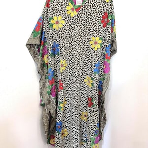 May include: A long, flowing kaftan dress with a V-neck, featuring a brown and white animal print. The dress is adorned with colorful floral accents in yellow, red, blue, and pink. The sleeves have a patterned trim.