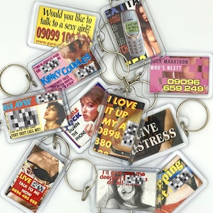 May include: A collection of clear acrylic keychains with various images and text. The keychains feature images of women, phones, and text such as "Would you like to talk to a sexy girl?" and phone numbers. The keychains are attached to silver key rings.
