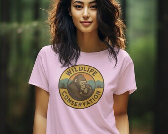 May include: A light pink t-shirt featuring a circular graphic with the words "Wildlife Conservation" and an illustration of a gorilla and baby. The shirt is worn by a person in a forest setting.