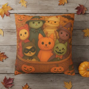 May include: Square orange Halloween cushion featuring a basket filled with cartoon cats in costumes. The cats are dressed as a mummy, witch, pumpkin, and more. The cushion has a pumpkin and bat design.