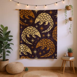 May include: A dark purple wall hanging featuring a repeating pattern of gold pangolins and star shapes. The pangolins are stylized with overlapping scales. The wall hanging is displayed on a wooden rod, adding a touch of natural warmth to the design.