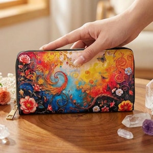 Op de afbeelding: Een kleurrijke portemonnee met ritssluiting en een levendig bloemen- en vlinderontwerp. De portemonnee heeft een zwarte rits en een goudkleurige trekker. Het kunstwerk bevat rode, oranje, gele, blauwe en witte tinten, waardoor een grillige en artistieke esthetiek ontstaat.