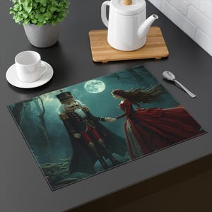 May include: A rectangular placemat featuring a fantasy scene with a Nutcracker figure in a black uniform and a woman in a red dress holding hands under a full moon. The background shows a dark forest.