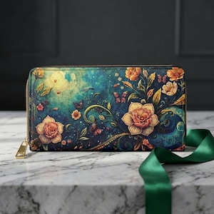 Op de afbeelding: Een portemonnee met ritssluiting met een bloemenontwerp. De portemonnee heeft een levendige illustratie van oranje bloemen, vlinders en bladeren tegen een teal en blauwe achtergrond. Een gouden rits en trekker maken het ontwerp compleet. Een groen lint staat op de voorgrond.