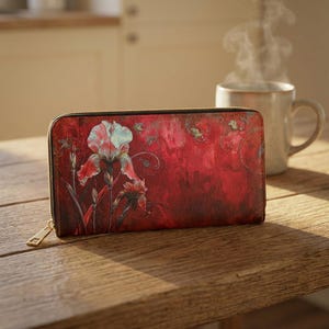 May include: A red floral wallet with a gold zipper. The wallet features a detailed illustration of an iris flower in shades of red, white, and green. The wallet is rectangular and appears to be made of leather or a similar material.